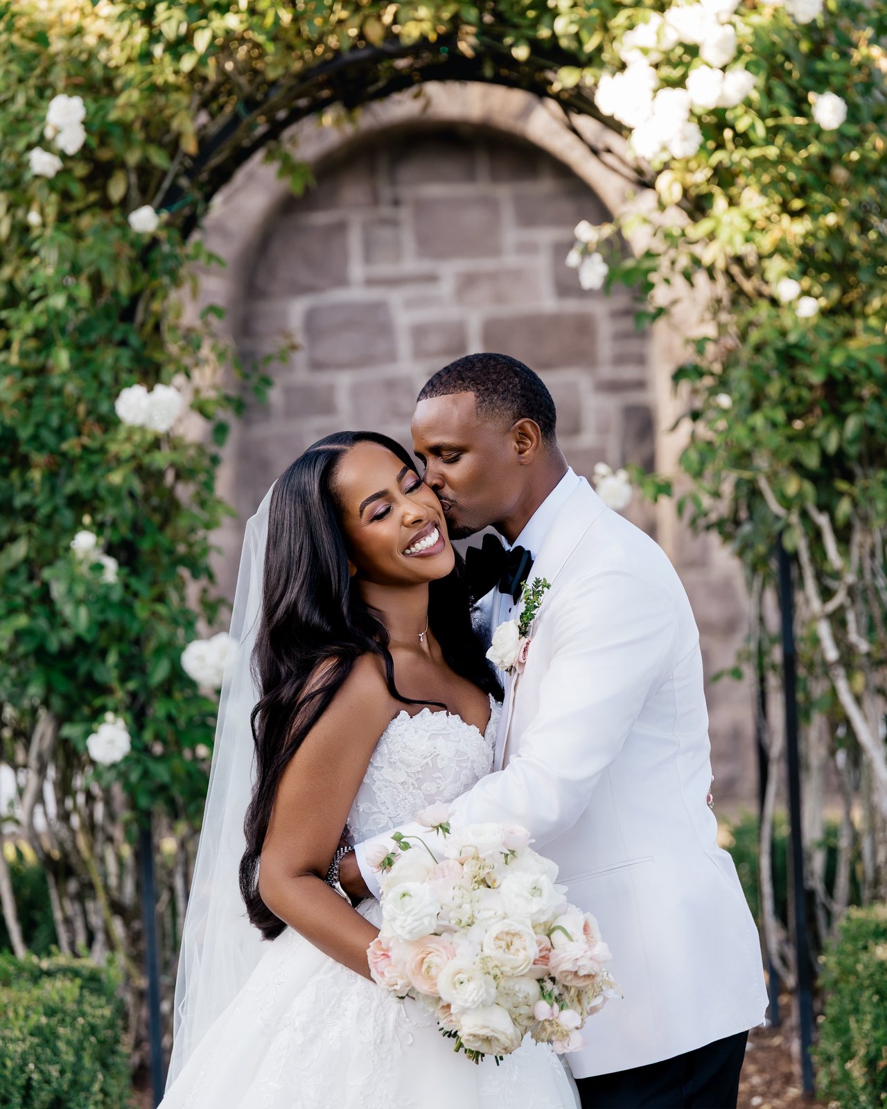 Wedding couple under rose arch — bridal makeup and hair by Sia Mia